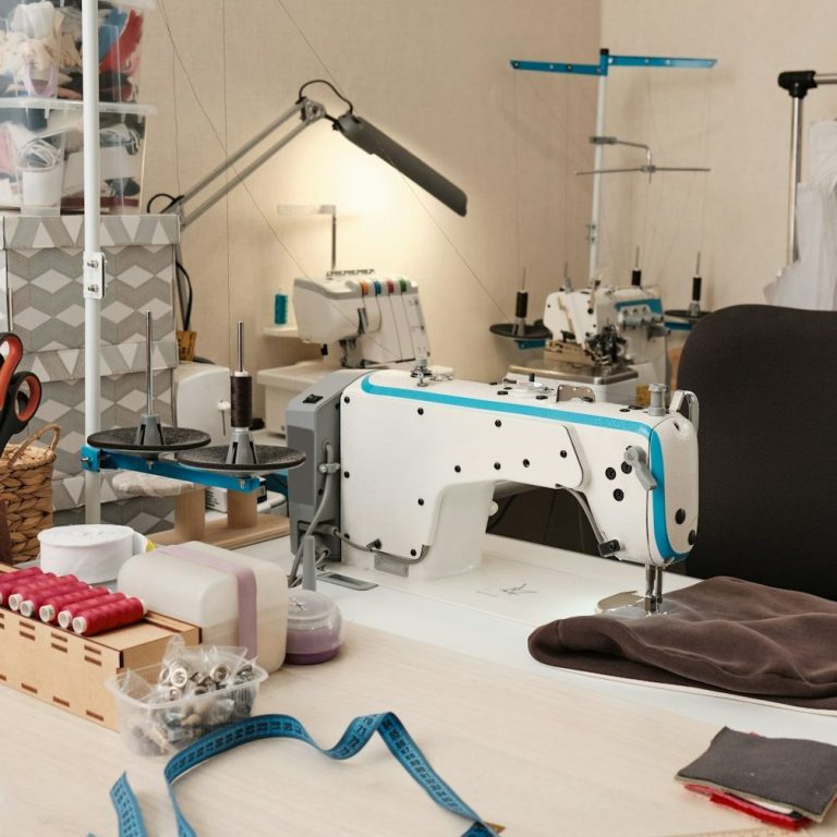 Unser Arbeitsbereich Nähmaschine und Zubehör auf einem Tisch, umgeben von Stoffen und Werkzeugen.